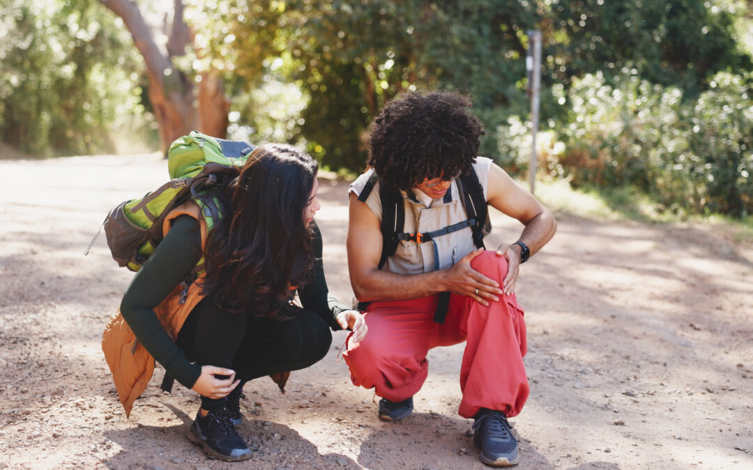 Man, knee pain and hiking with partner in forest for adventure with fatigue, injury or discussion on trail. People, talk and sore joint with stress, inflammation and rest with burnout with trekking.